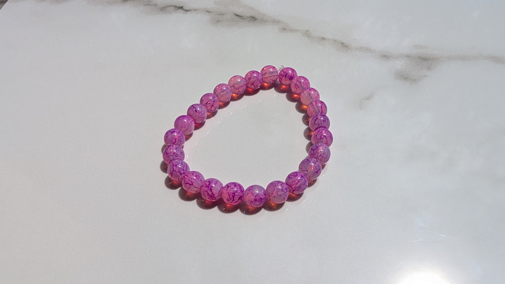 Fushcia beaded stretch bracelet laid out flat on whit marbled tile 