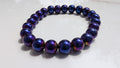 A beaded stretch bracelet made of glossy, mettalic dark purple beads with blue and violet, gold shifts, resting on a white surface.