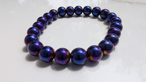 A beaded stretch bracelet made of glossy, mettalic dark purple beads with blue and violet, gold shifts, resting on a white surface.