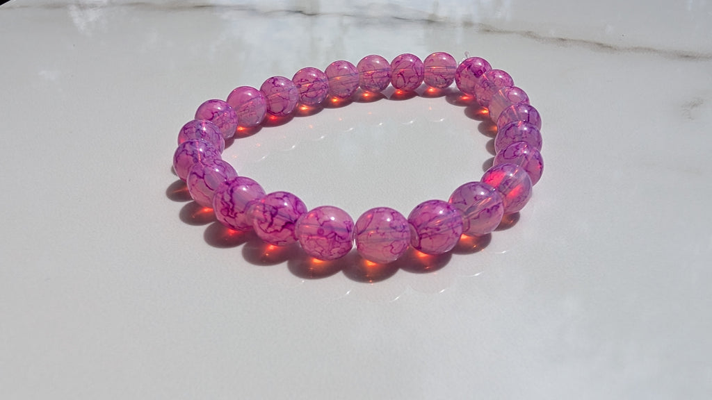 Fushcia beaded stretch bracelet laid out flat on white marbled tile