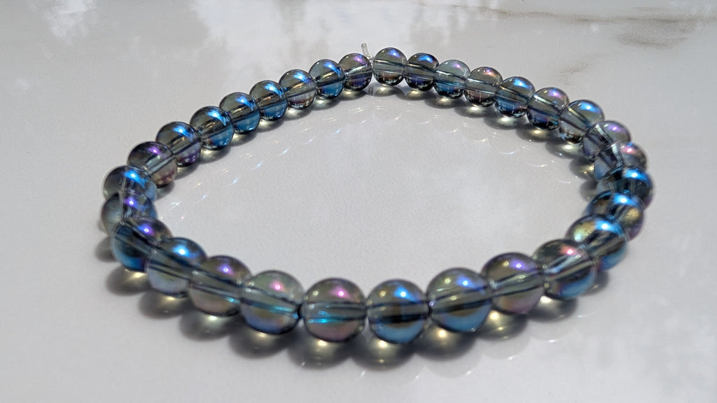 A beaded stretch bracelet with dark gray metallic beads and iridescent blue-purple accents, resting on a white marble surface.