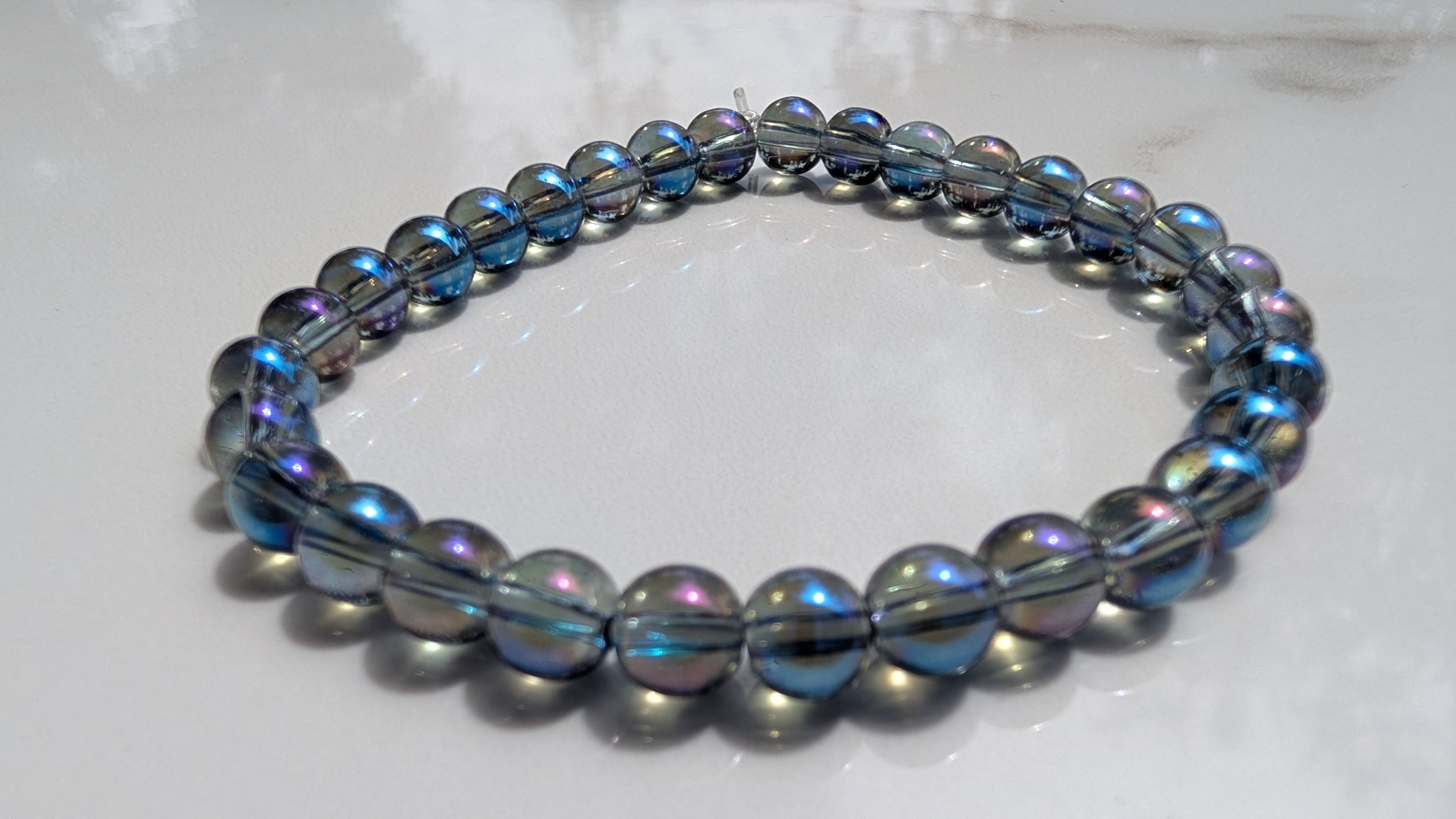 A beaded stretch bracelet with dark gray metallic beads and iridescent blue-purple accents, resting on a white marble surface.