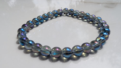 A beaded stretch bracelet with dark gray metallic beads and iridescent blue-purple accents, resting on a white marble surface.